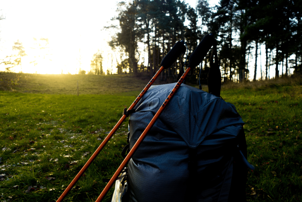 hiking poles resting against a blue backpack in a clearing at sunset