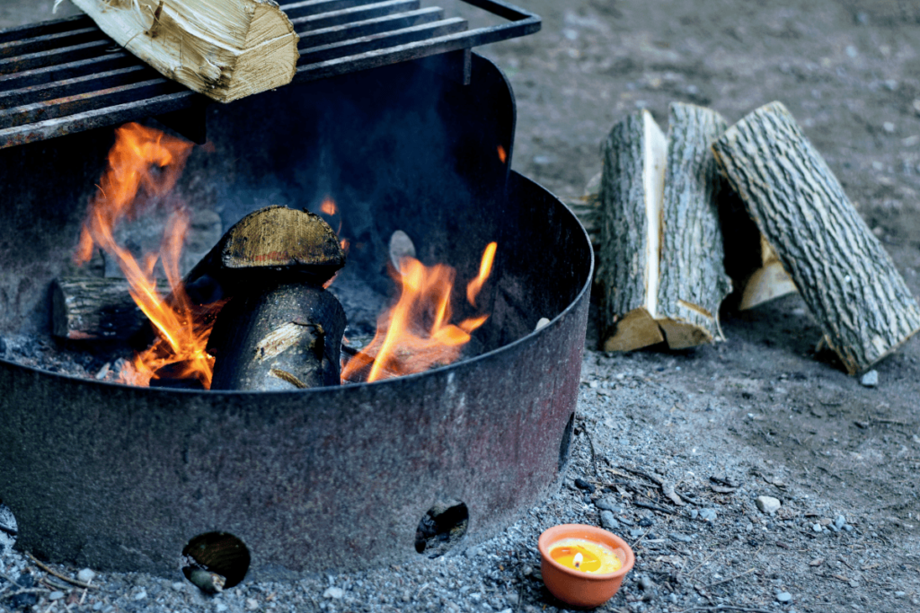 a photo of a fire pit with logs, flame  and campfire smoke